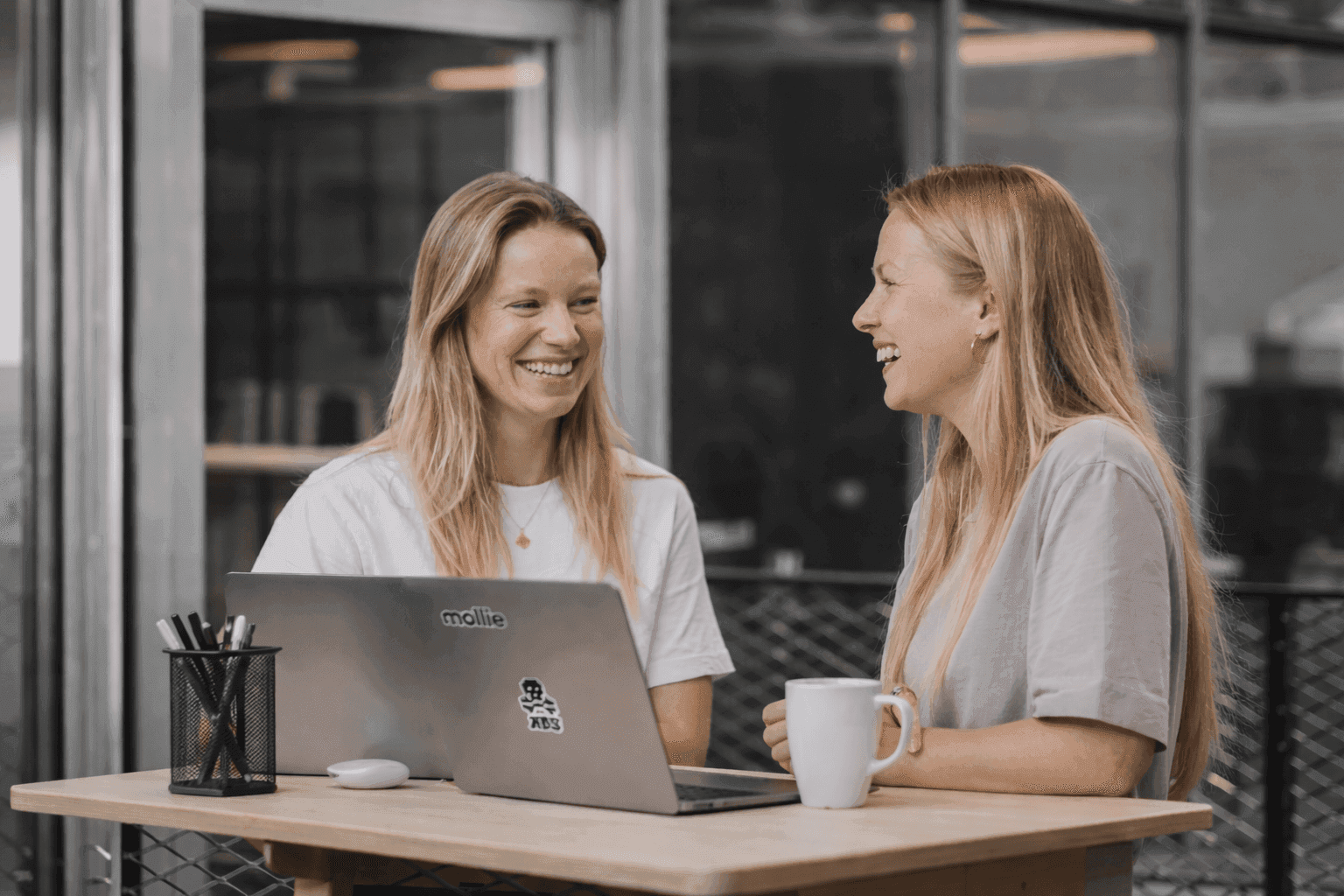 Twee collega's overleggen lachend achter een laptop op kantoor